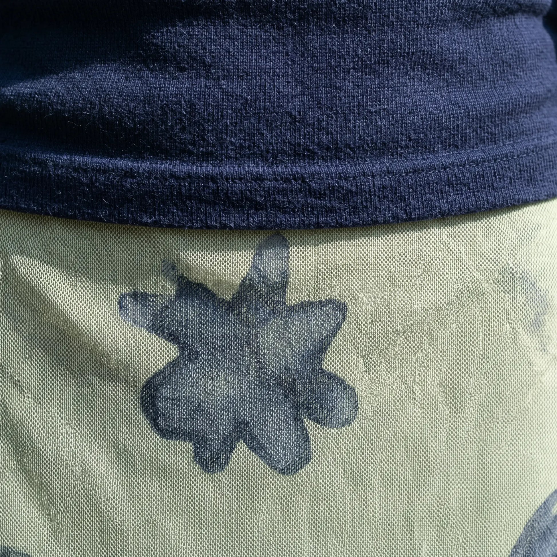 Close-up detail of the deep navy knit fabric from the V-neck top and the pale sage green mesh overlay of the maxi skirt with dark abstract patterns.