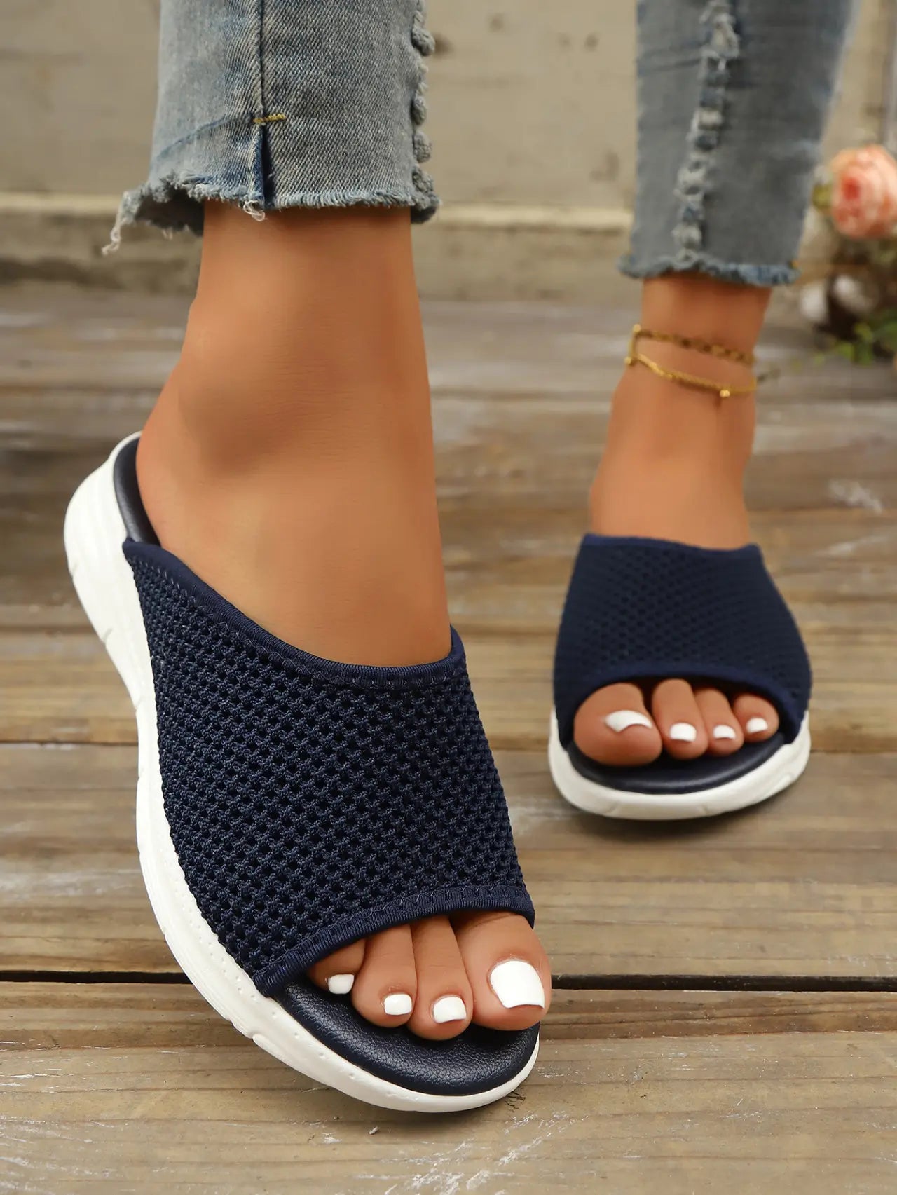 Navy blue breathable knit slide sandals worn by a woman with white-painted toenails, showcasing the slip-on design and contoured footbed on a wooden deck.