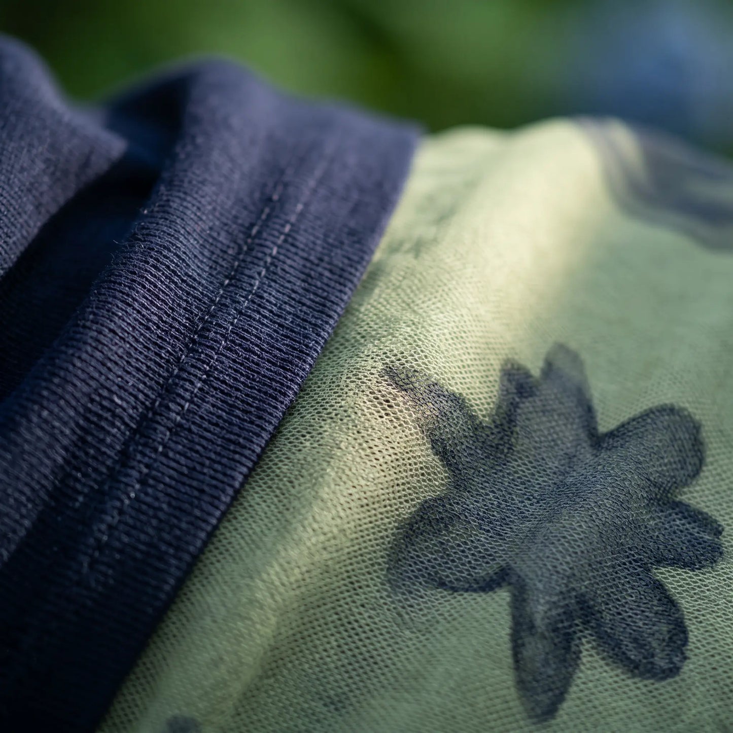Close-up detail of the dark navy knit V-neck top fabric next to the pale sage green mesh maxi skirt, featuring an intricate navy abstract starburst pattern.