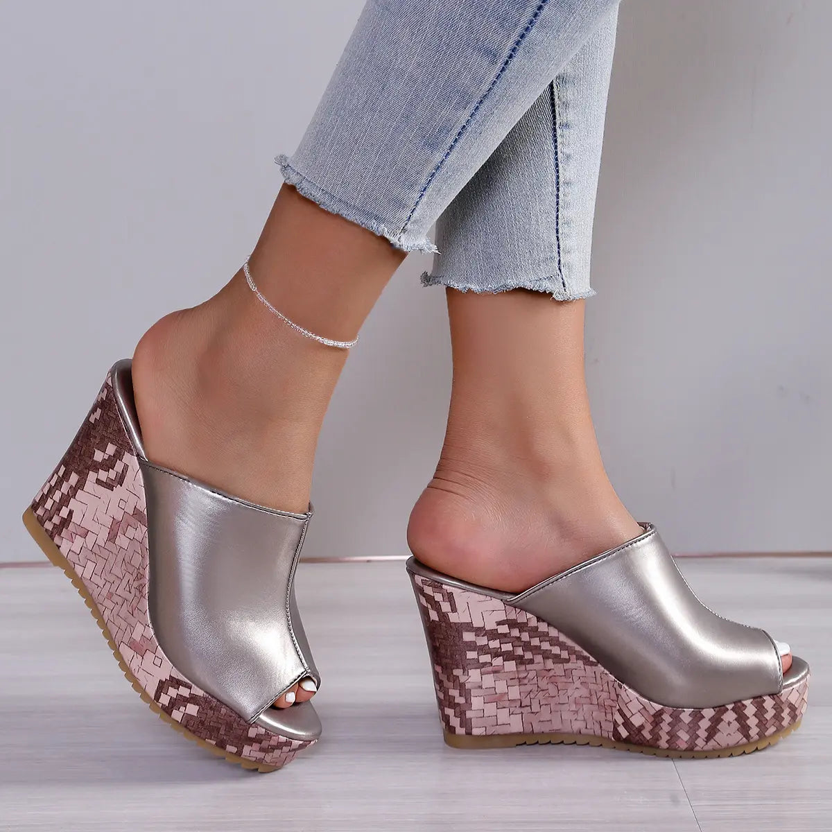 Nuvira metallic silver peep-toe wedge sandals with a textured rose gold patterned wedge heel, worn by a model with light blue jeans and a delicate anklet.