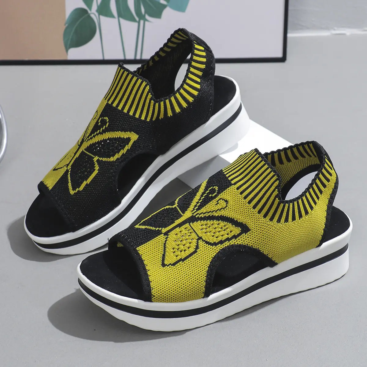 Nylira women's black and yellow knitted wedge sandals with a detailed butterfly embroidery and peep-toe design.