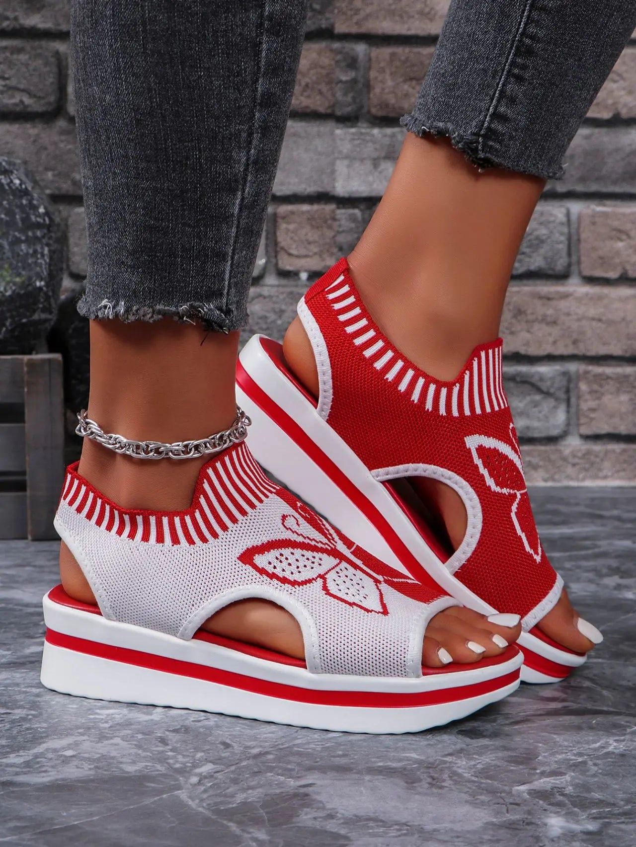 Women's red and white knitted wedge sandals with a white butterfly embroidery and a slingback strap, styled with grey jeans.