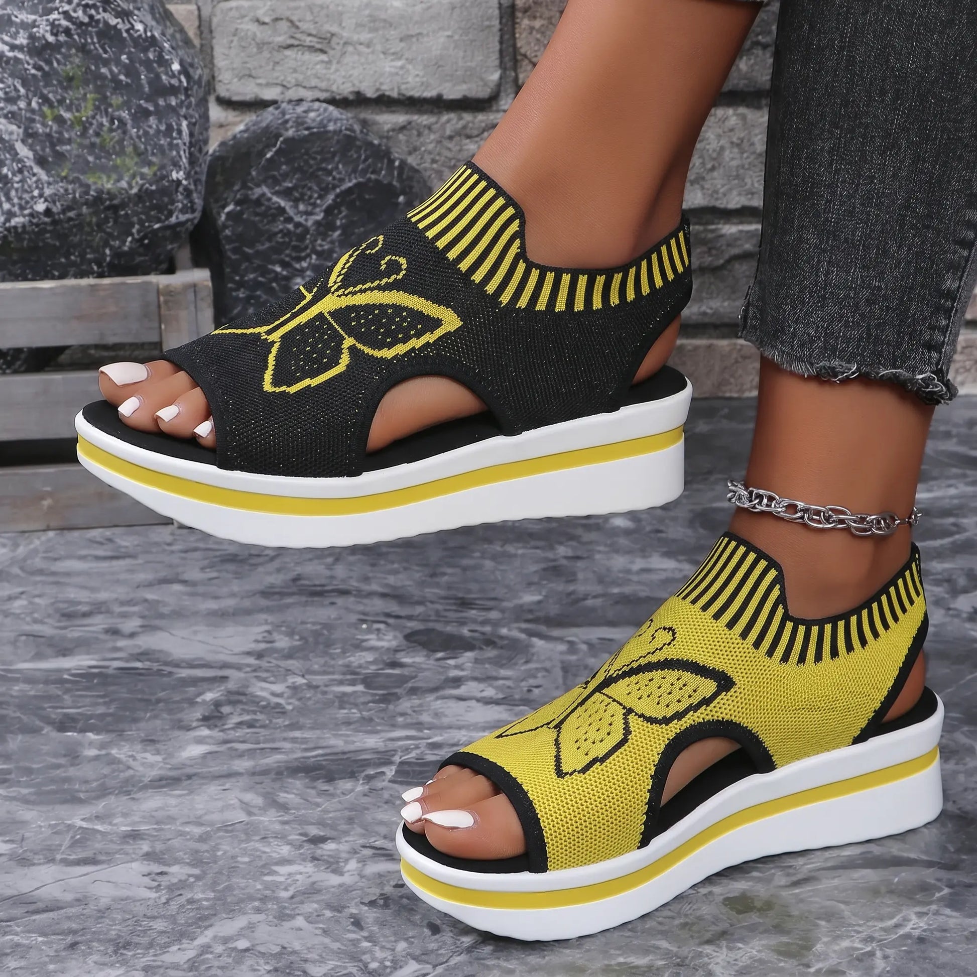 Nylira women's peep-toe wedge sandals in sunny yellow, featuring intricate black butterfly embroidery, a striped elastic collar, and a layered foam sole with a slingback strap. White-tipped toes are visible.