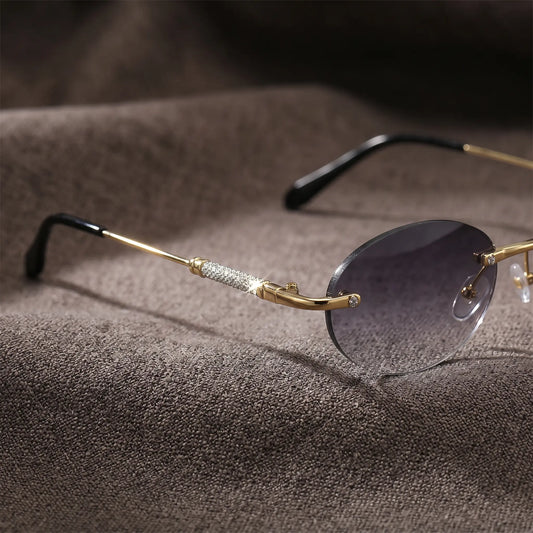 Close-up of Nymira oval rimless sunglasses, showcasing gold-toned metal temples adorned with sparkling clear crystals and black acetate ear tips, with a dark grey gradient lens.