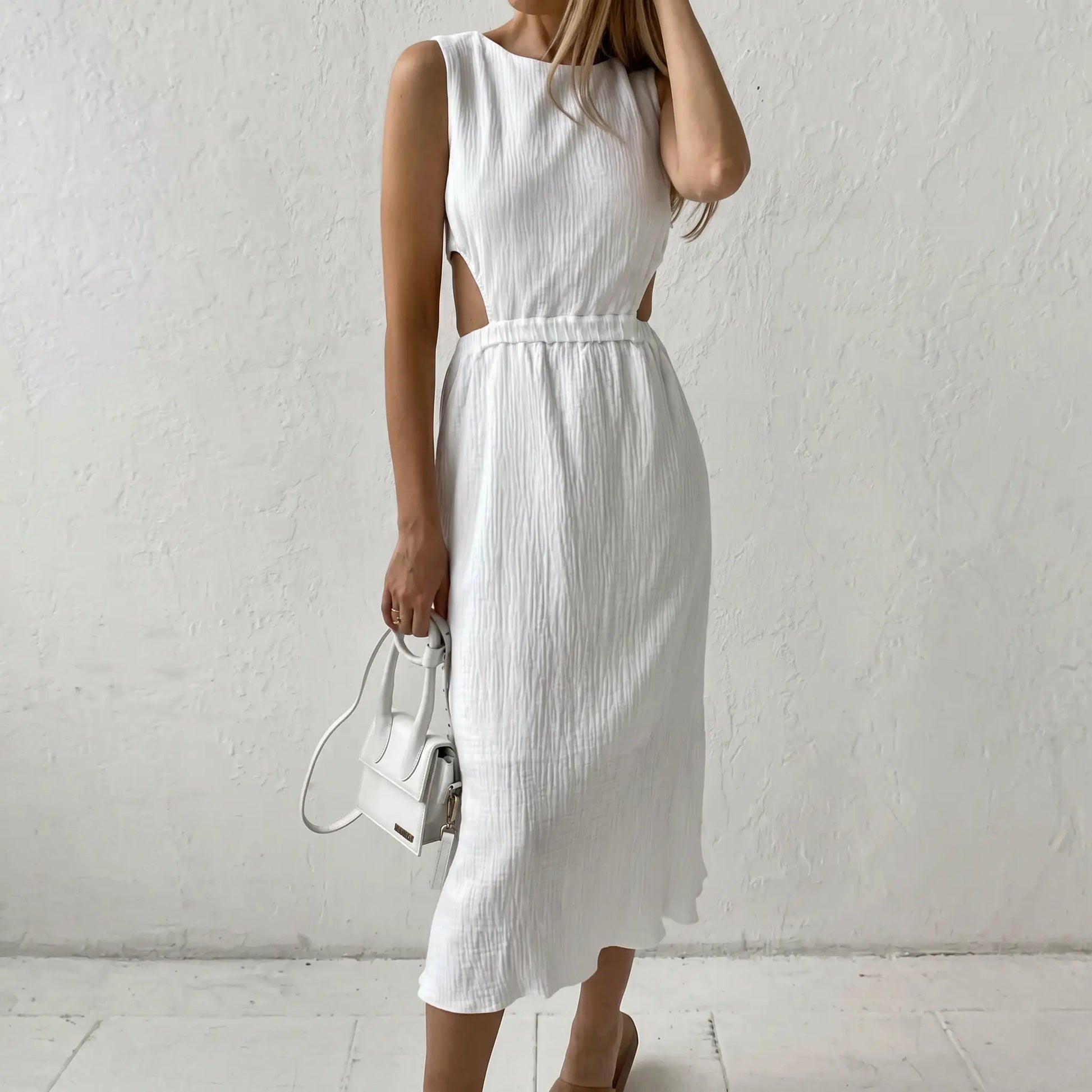 White sleeveless cotton bubble crepe midi dress with round neckline and distinctive side waist cut-outs, displayed on a model against a neutral textured background.