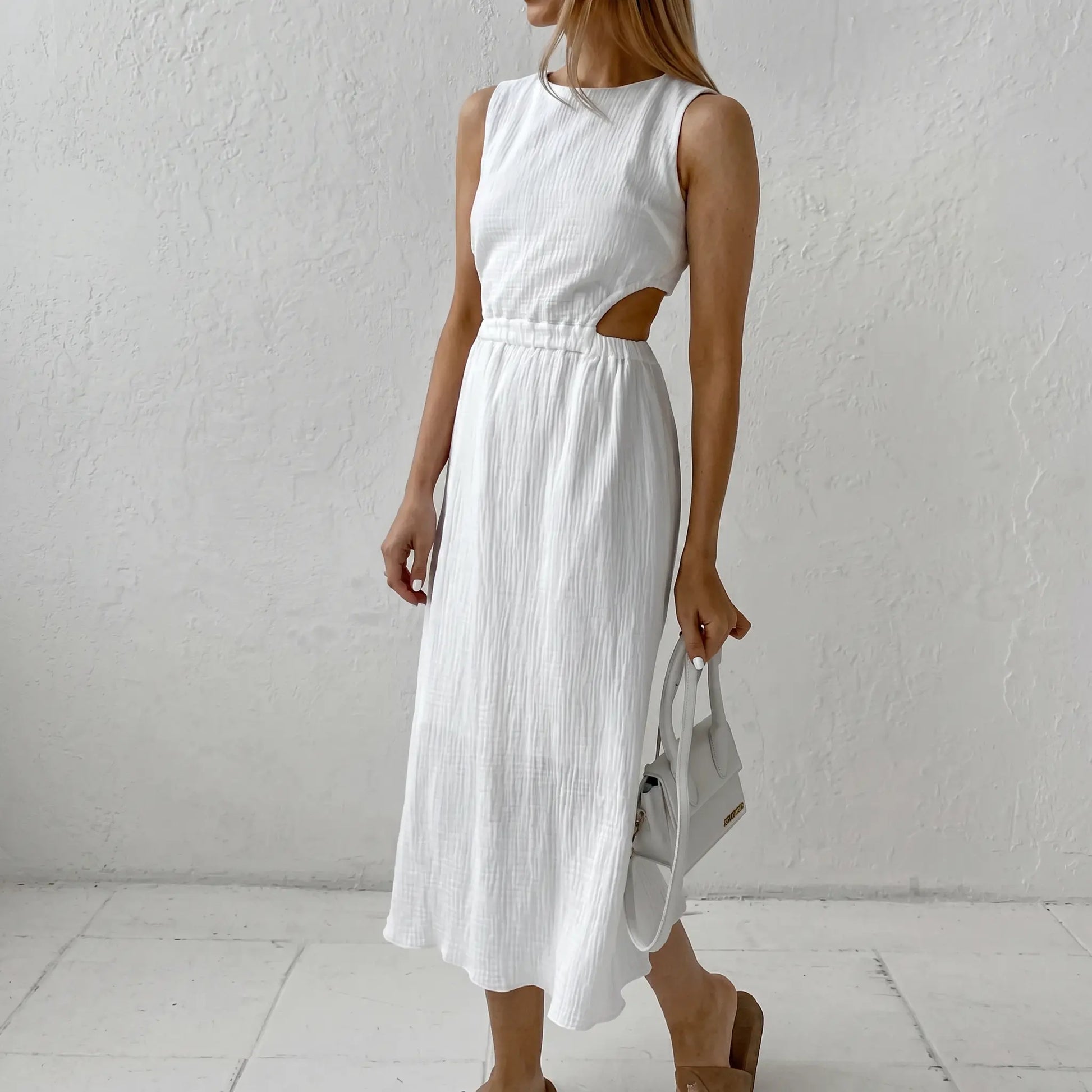 Nyssa white cotton bubble crepe midi dress featuring a round neckline, sleeveless design, and striking side waist cut-outs, shown on a model against a textured studio background.