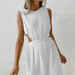 Nyssa white cotton crepe sleeveless midi dress featuring a round neckline, elasticated waist with side cut-outs, and a straight mid-calf skirt, shown on a model against a textured off-white studio background.