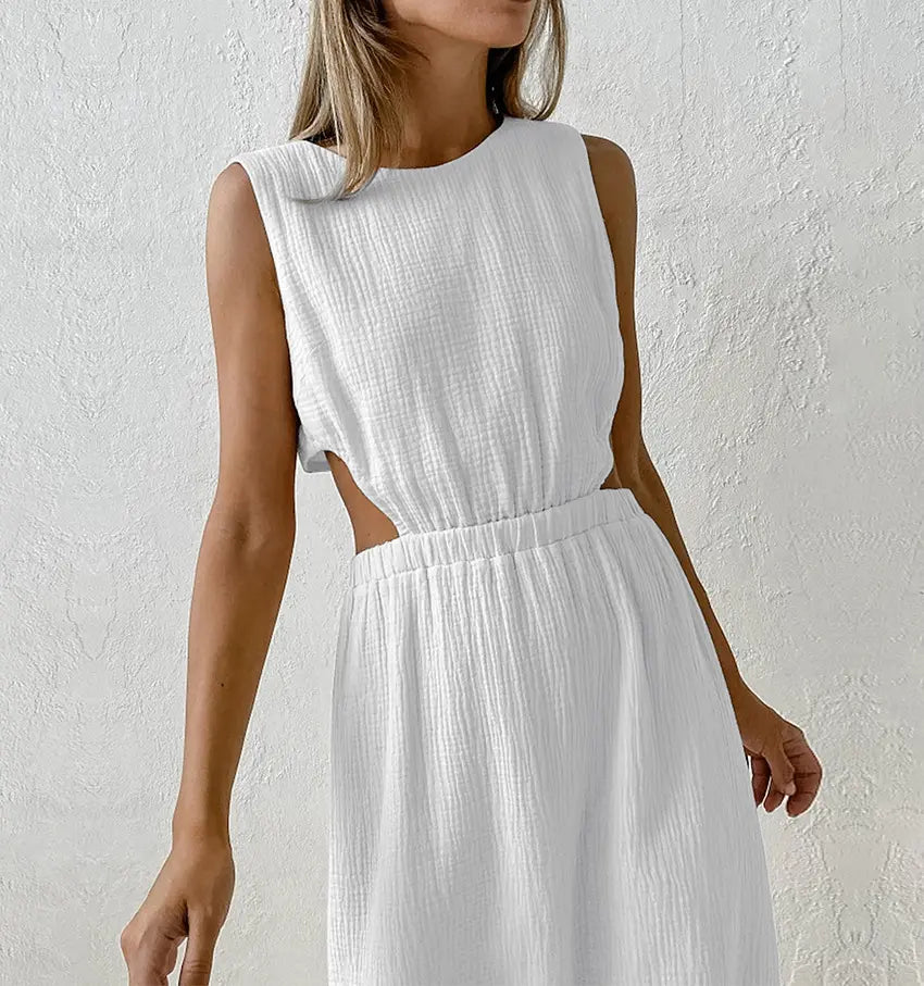 Nyssa white cotton crepe sleeveless midi dress featuring a round neckline, elasticated waist with side cut-outs, and a straight mid-calf skirt, shown on a model against a textured off-white studio background.
