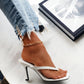 White Nyxos stiletto thong sandals with a square toe, worn by a model with distressed denim jeans and a gold anklet against a marble surface.