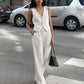 A woman models a pristine white sleeveless V-neck vest and flowing wide-leg trousers set, standing on a city street with a handbag.