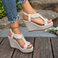 Close-up of off-white bohemian wedge sandals with intricate pearl and crystal embellishments on the T-strap, worn with distressed denim jeans. Features a high wedge heel covered in textured fabric and an elasticized ankle strap.
