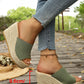 Olive green knitted espadrille wedge sandals with a platform sole and open toe, shown on feet styled with blue denim jeans on a wooden boardwalk.