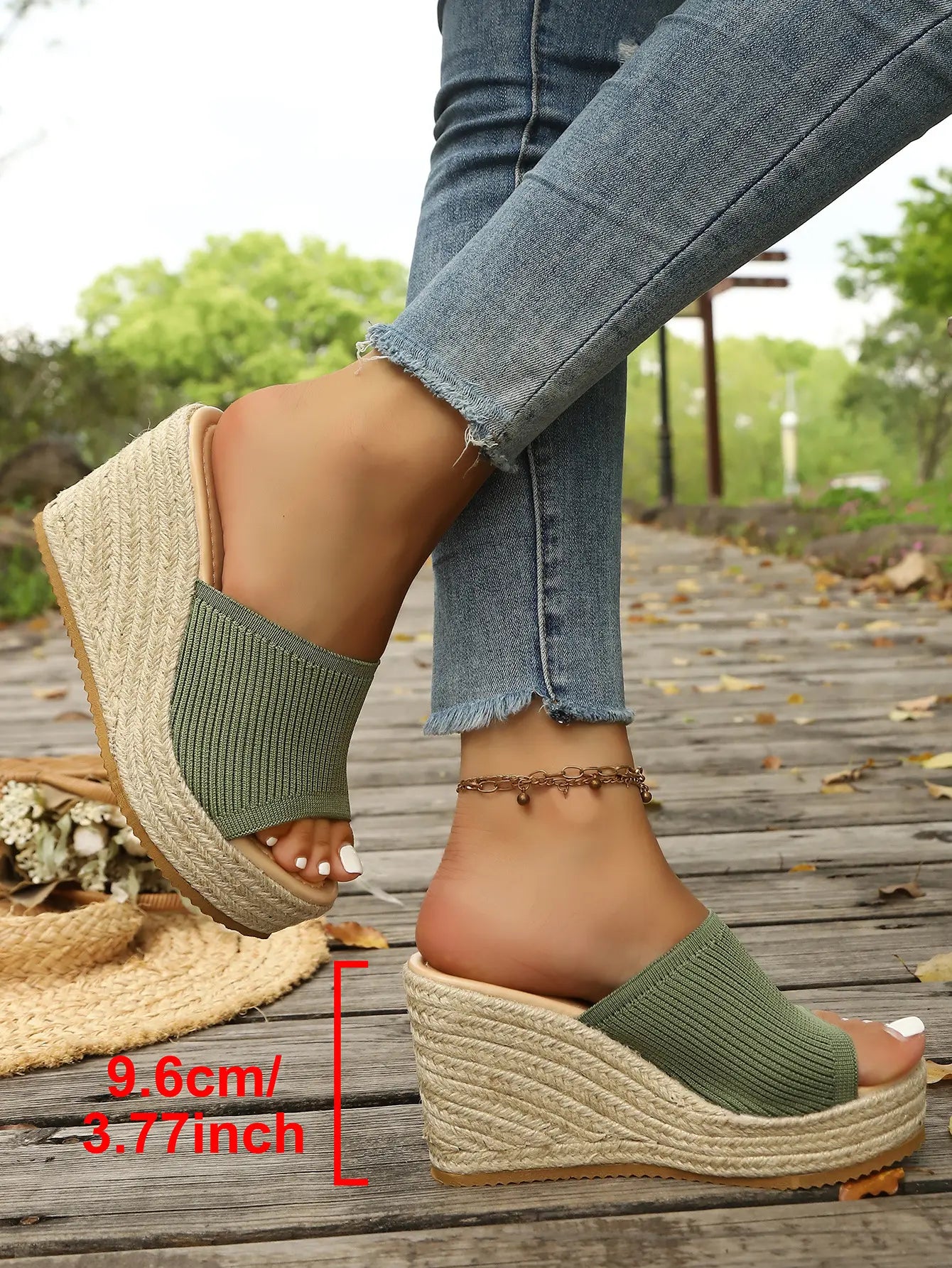 Olive green knitted espadrille wedge sandals with a platform sole and open toe, shown on feet styled with blue denim jeans on a wooden boardwalk.
