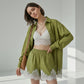 Olive green linen-blend relaxed-fit shirt and wide-leg shorts set adorned with delicate white lace trim on the shorts hem and shirt placket, modeled by a woman in a studio.
