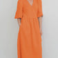 A woman models an orange cotton gauze midi wrap dress with short puff sleeves and a tie waist, offering a relaxed bohemian silhouette.