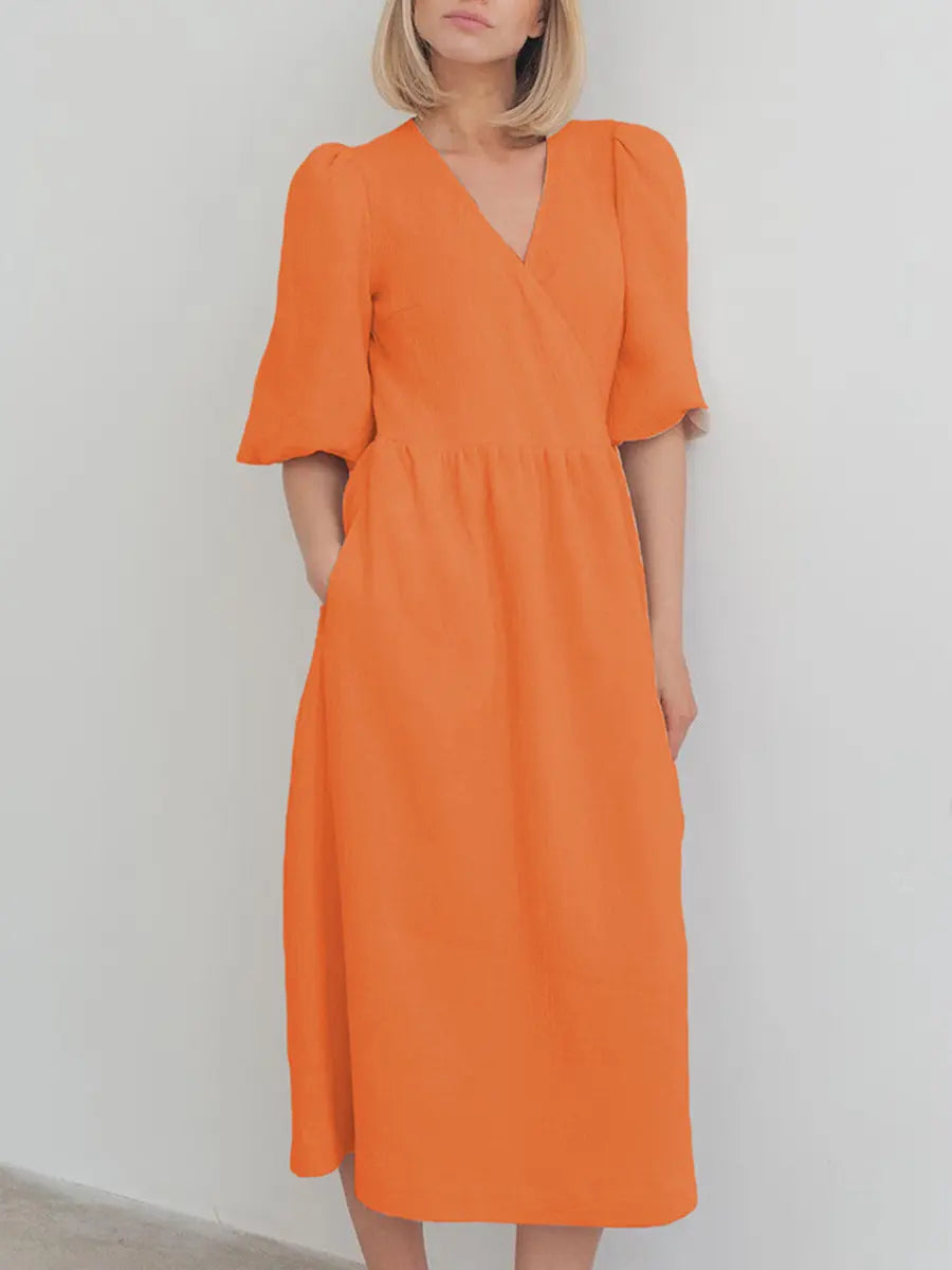 A woman models an orange cotton gauze midi wrap dress with short puff sleeves and a tie waist, offering a relaxed bohemian silhouette.