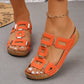 Orange platform wedge sandals with geometric gold-tone embellishments and white contrast stitching, worn on a foot with white pedicure and pearl anklet.
