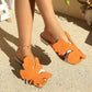Vibrant orange bohemian flat sandals with large leaf embellishments and crystal-adorned low block heels, worn by a model outdoors.