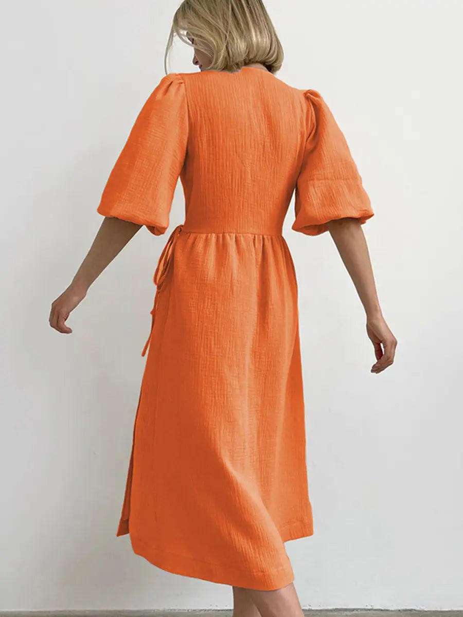 Orange crinkled cotton gauze midi wrap dress with short puff sleeves and tie waist, shown from the back view on a model against a white background.