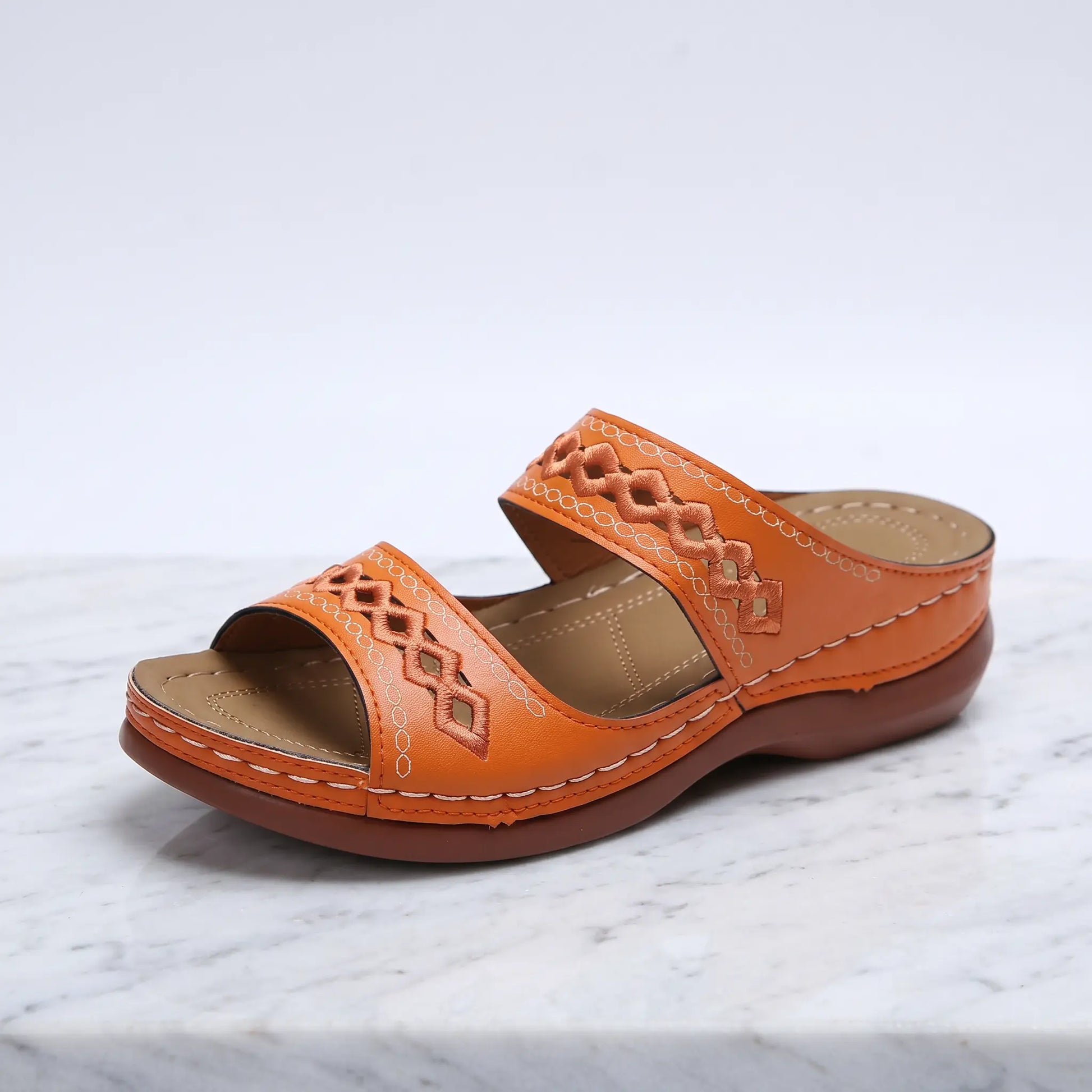 Vibrant tangerine peep-toe wedge sandal with two wide straps featuring geometric diamond cut-outs and white contrast stitching, shown at a three-quarter angle.