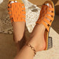Elegant orange woven flat slide sandals worn by a model, showcasing intricate basket-weave straps and an embellished low block heel, styled for a bohemian summer look.