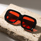 Kyzeth oversized square sunglasses with a high-gloss black frame and vibrant crimson red lenses, displayed on a textured beige travertine block.