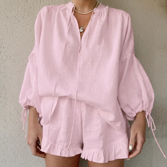 Pale pink linen-blend loungewear set featuring a loose V-neck blouse with voluminous lantern sleeves and ruffled hem shorts, worn by a model.
