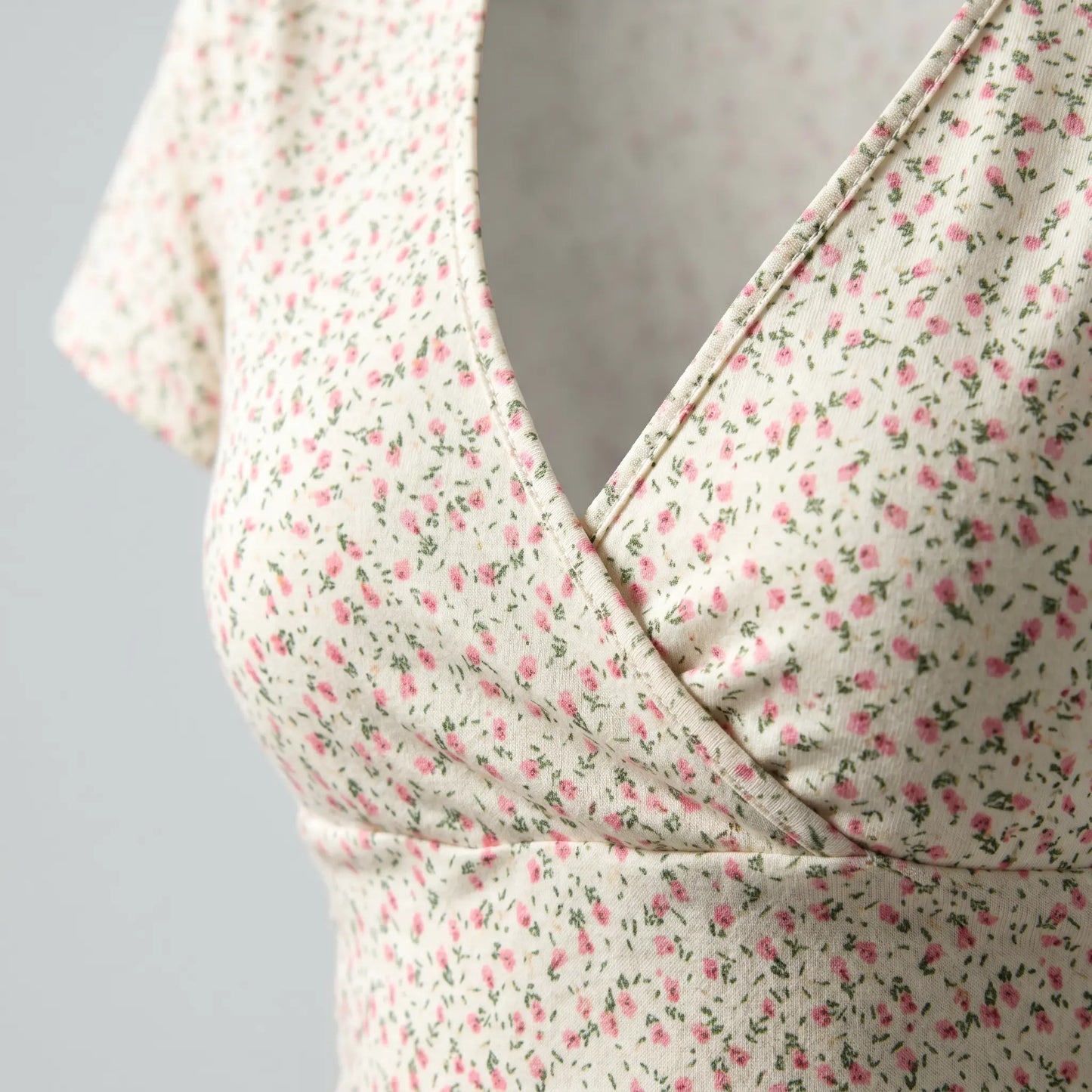 Close-up of the Brivan Pearl White floral V-neck crop top, highlighting its delicate pink blossom pattern, smooth stretch fabric, and elegant faux-wrap neckline with a fitted underbust band.