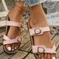 Elegant pink cork footbed slide sandals with adjustable antique brass buckle straps, worn by a woman with white painted toenails and ripped jeans.