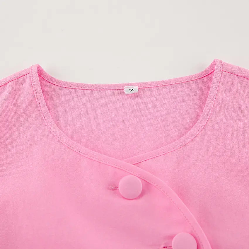Close-up of a vibrant pink cotton button-up top featuring fabric-covered buttons and a flattering round neckline with a size label.