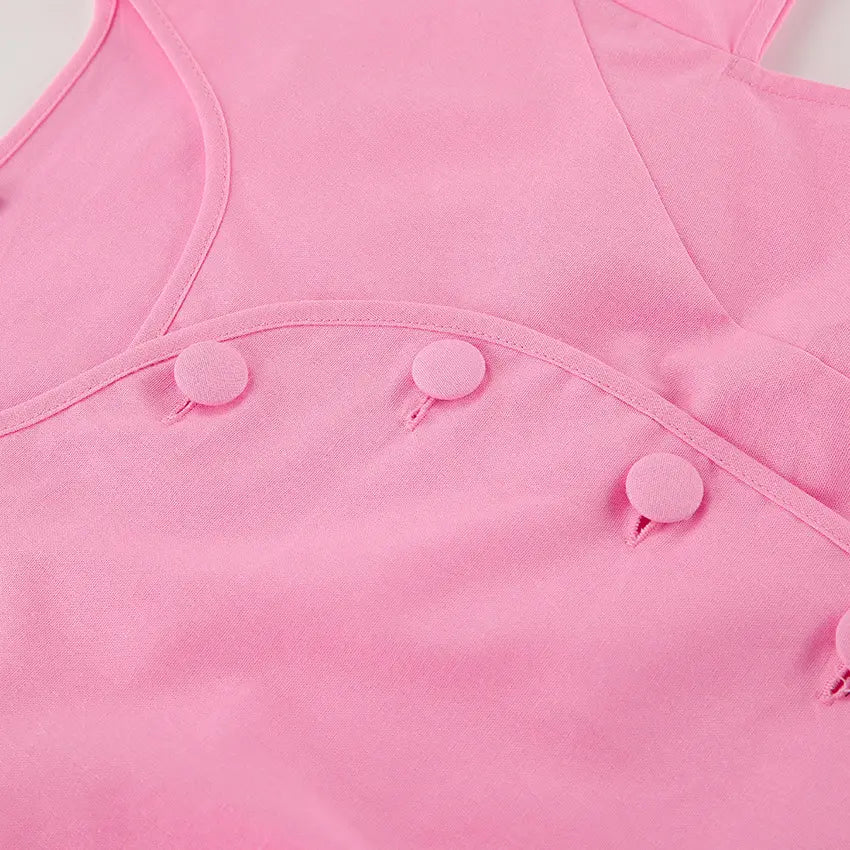 Close-up detail of a vibrant pink cotton two-piece set, showcasing matching fabric-covered buttons on the rounded neckline and front placket of a cropped top and midi skirt.