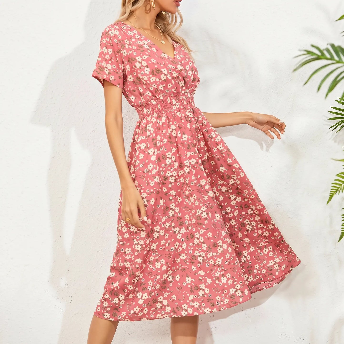 A woman models a pink ditsy floral midi dress featuring a V-neck, short flutter sleeves, and a cinched smocked waist with a flowy A-line skirt.