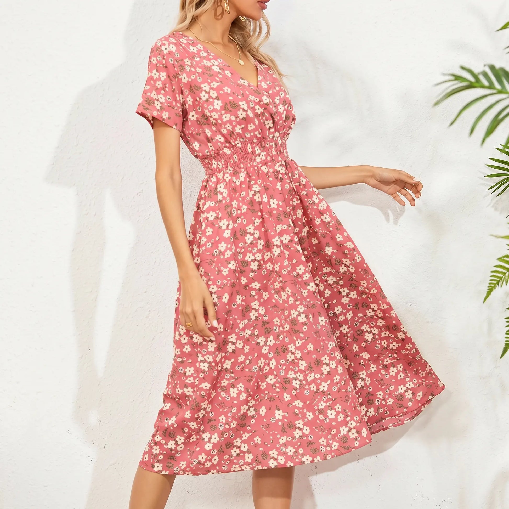 A woman models a pink ditsy floral midi dress featuring a V-neck, short flutter sleeves, and a cinched smocked waist with a flowy A-line skirt.