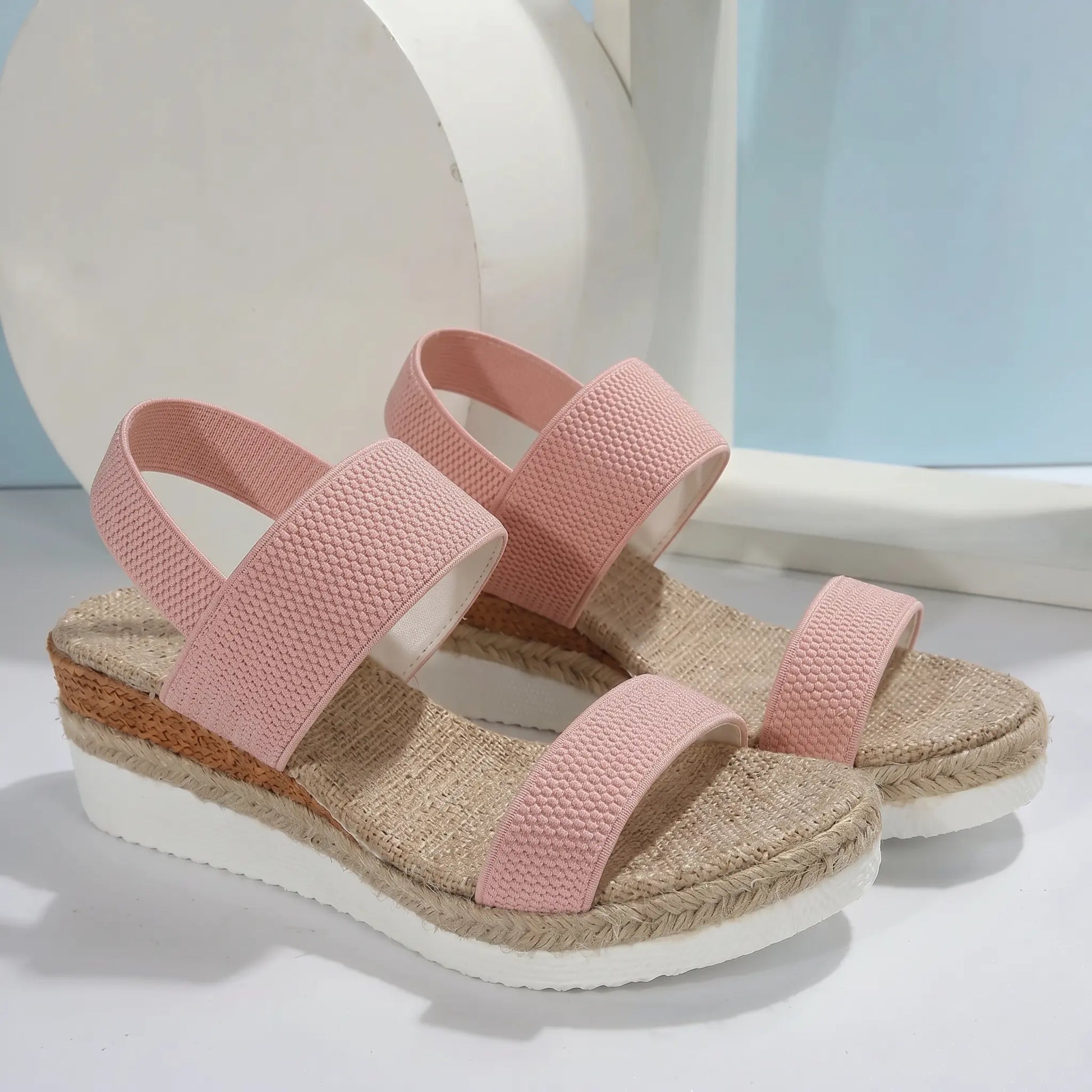 Blush pink woven fabric espadrille wedge sandals with a natural jute-wrapped platform and elasticated slingback strap, shown from a three-quarter front view on a studio background.