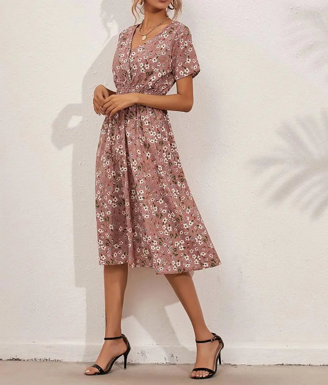 A woman models a pink ditsy floral print V-neck midi dress with short flutter sleeves and a cinched elasticated waist, paired with black high-heeled sandals. The dress falls to mid-calf.