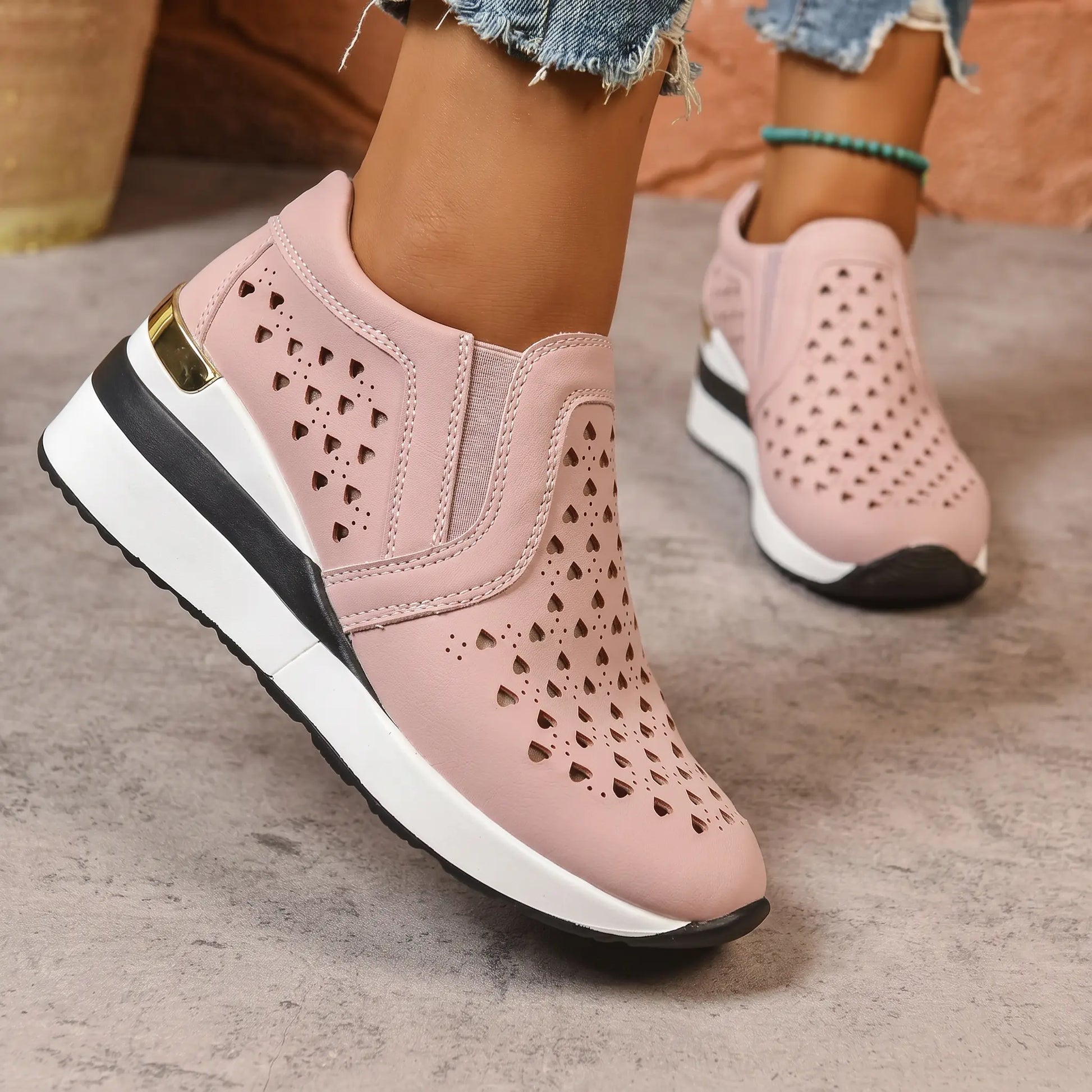 Pink perforated heart slip-on wedge loafers worn by a model, showcasing the three-quarter front view with a subtle gold heel accent.