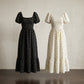 Front view of two Buzalo Romantic Polka Dot Smocked Maxi Dresses: one black with white polka dots and one ivory with black polka dots. Both feature square necklines, smocked bodices, short puff sleeves, and tiered ruffle hems.