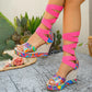 Vibrant multicolor psychedelic swirl platform wedge sandals with hot pink elastic gladiator lacing wrapping the leg. Features a peep-toe front, espadrille wedge, and rear zipper, shown in a bohemian-inspired outdoor setting.