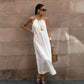 Model wearing Qyren's flowing ivory-white halter maxi dress with ruched neckline and A-line silhouette, styled elegantly against a textured stone wall.