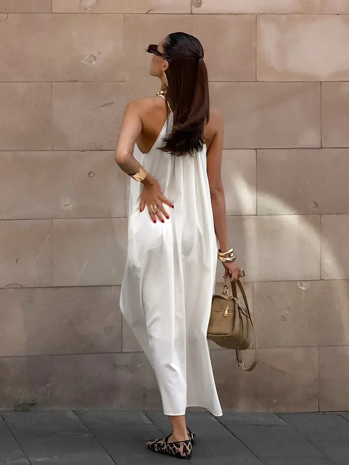 Qyren ivory white flowing halter resort maxi dress, worn by a model from the back. Shows gathered halter neckline, delicate straps, open back, and sweeping A-line silhouette.