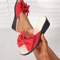 Red Lysa wedge slides featuring a large, soft bow detail on the single strap, shown on a foot with a black wedge heel and cream footbed against a studio background.