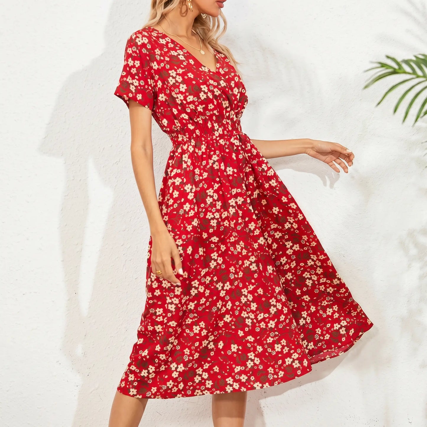 Red midi dress with a ditsy floral print, featuring a V-neck, short flutter sleeves, and a cinched smocked waist, shown on a model against a textured background with palm leaf shadows.