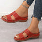 Side view of a model's foot wearing vibrant red Briska slip-on sandals featuring intricate laser-cut patterns, metallic stud accents, and a low wedge heel, paired with ripped blue jeans.