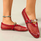 A pair of vibrant red mesh flat sandals with patent faux leather trim and decorative gold buckle straps, worn by a model on a neutral studio background, adorned with a beaded anklet.