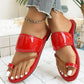 Red patent toe-thong flat sandals worn by a model with braided detail and a gold anklet, styled with denim jeans in a lifestyle setting.