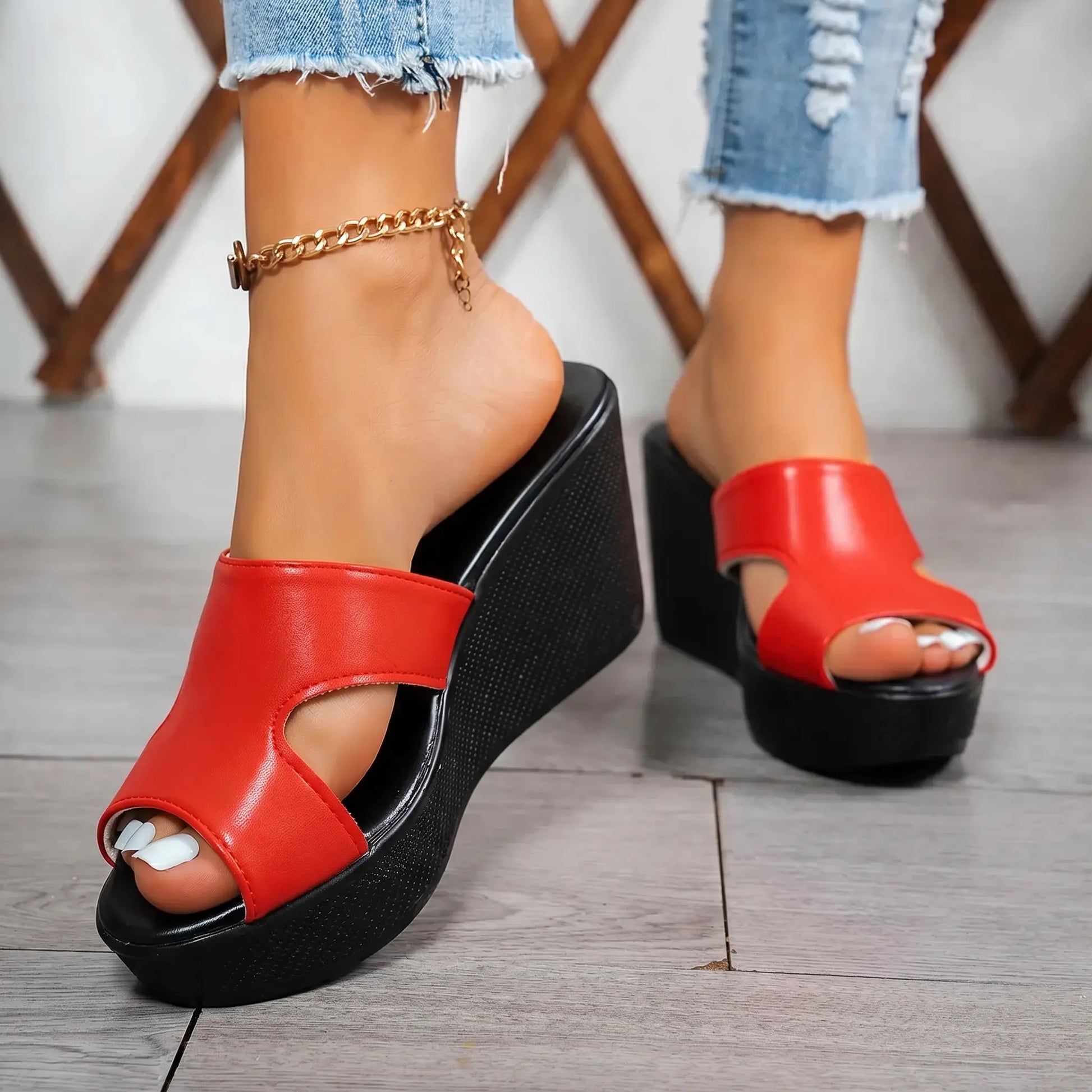 Red peep-toe wedge platform sandals with a single geometric cutout strap, worn by a model with ripped denim jeans and a gold anklet.