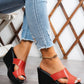 Elegant red peep-toe wedge sandals with a black textured sole and a single supportive strap, shown on a model's feet with ripped denim jeans and a gold anklet.