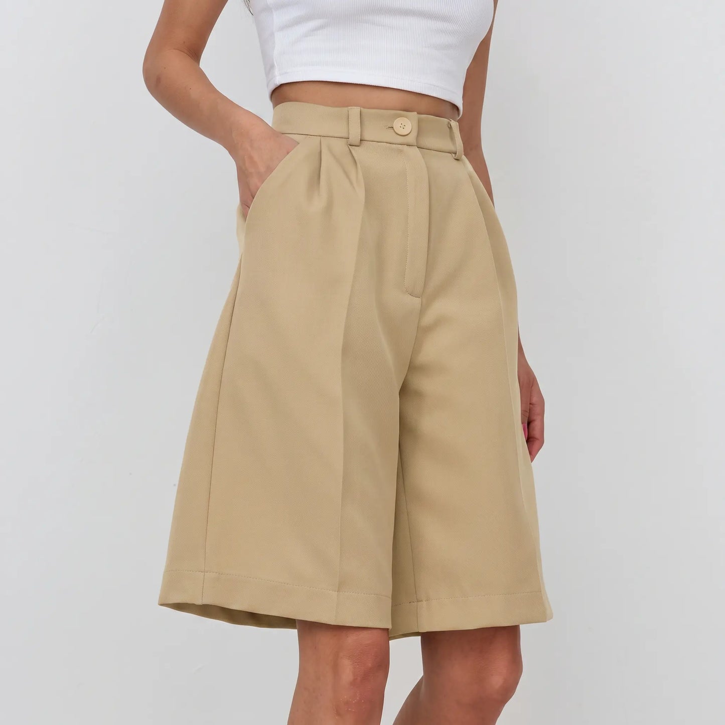 High-waisted, tailored Bermuda shorts in a warm khaki color, featuring wide legs, front pleats, and a smooth polyester blend fabric. Shown on a model against a white background.
