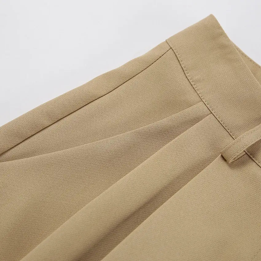Close-up view of high-waisted Rhyza Tailored Bermuda Shorts in Khaki, showcasing the smooth polyester blend fabric, crisp front pleats, and a visible belt loop.