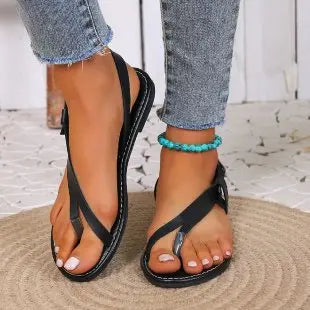 Black Rhyzak women's flat sandals featuring a toe loop design, adjustable ankle strap with silver buckle, and prominent white stitching on the black sole, worn on a model's feet with denim jeans.